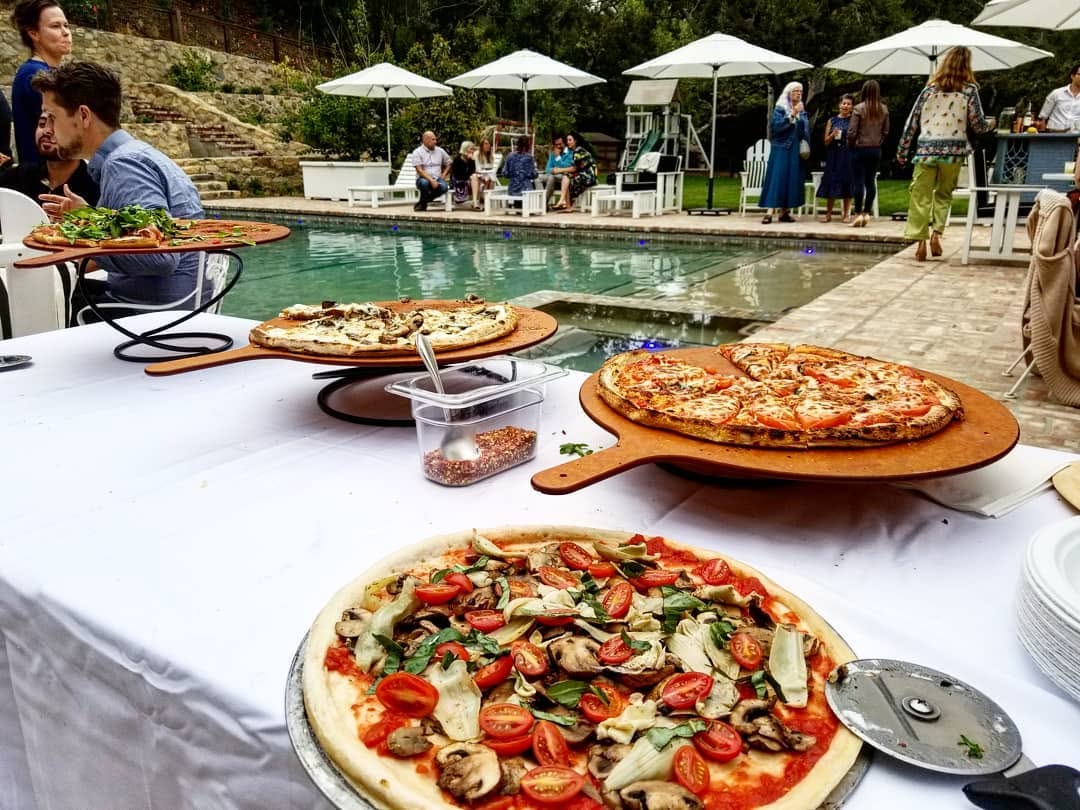 Poolside pizza catering station with artisan pizzas on wooden peels at a Los Angeles hillside home