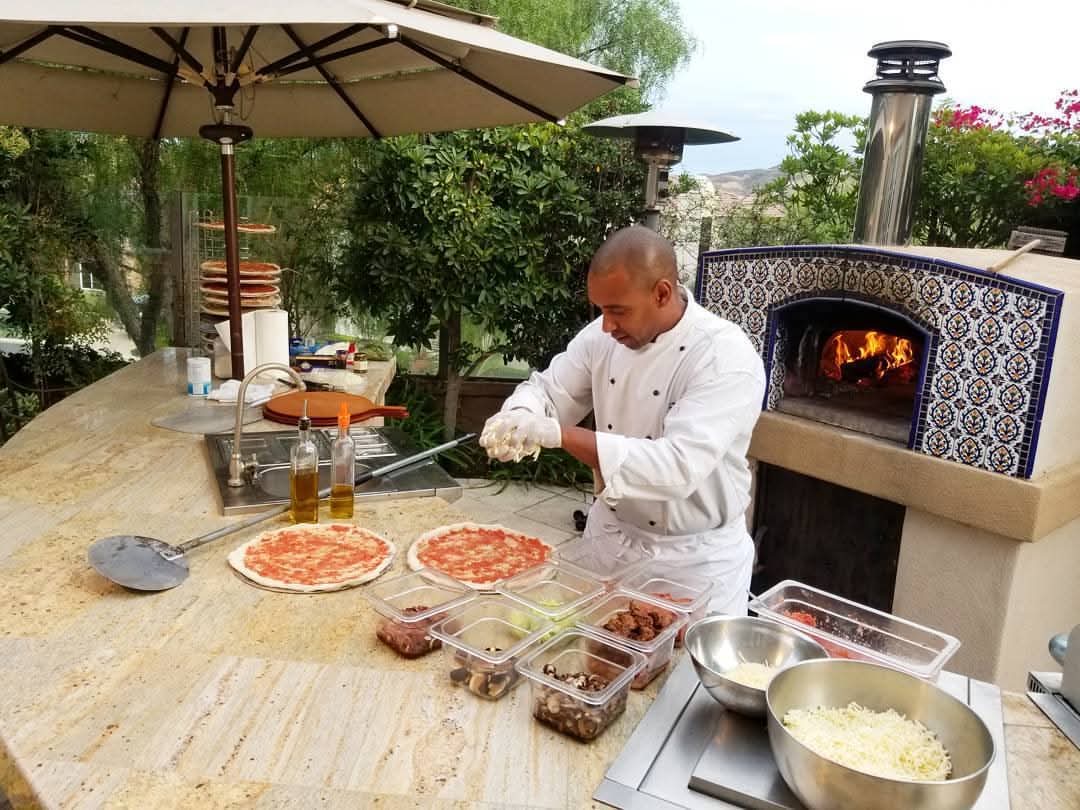 Executive chef stretching dough and dressing pizzas at a blue-tiled live-fire oven station at a Los Angeles estate event